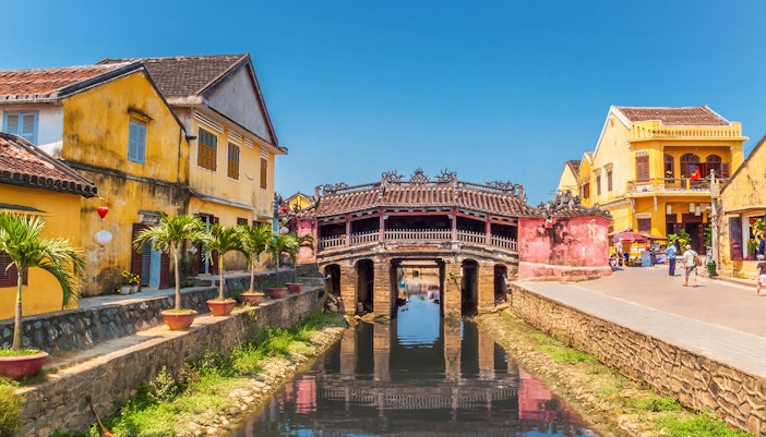 Japanese Covered Bridge over canal in Hoi An, Vietnam, with yellow buildings nearby.
