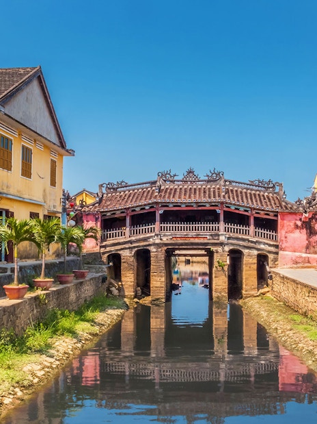 Japanese Covered Bridge over canal in Hoi An, Vietnam, with yellow buildings nearby.