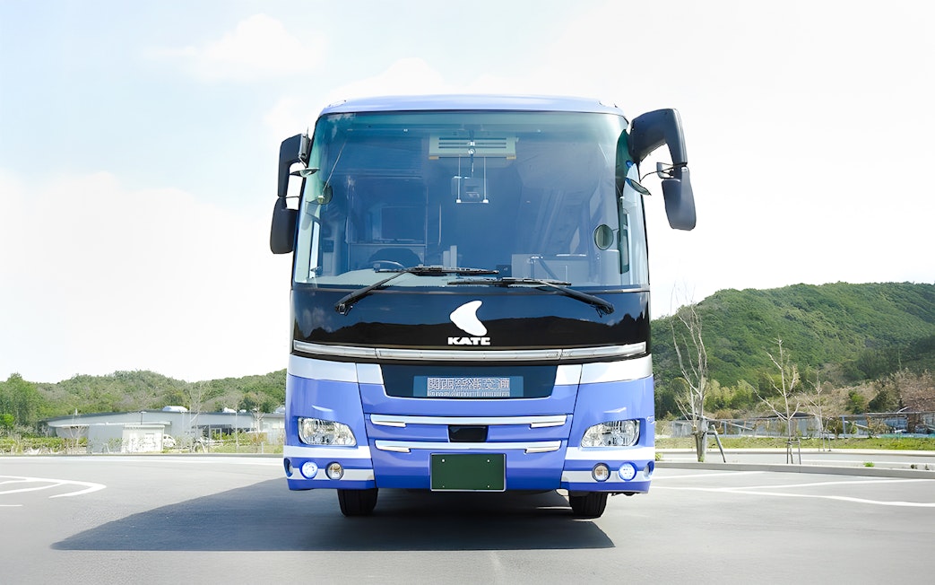 Kansai Airport transfer bus parked in lot with green hills in background.