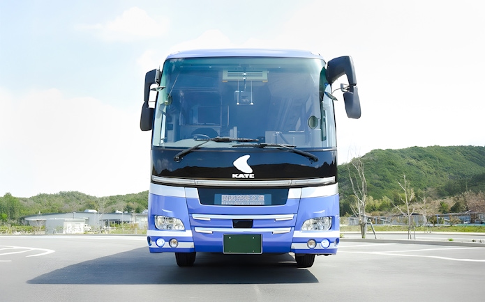Kansai Airport transfer bus parked in lot with green hills in background.
