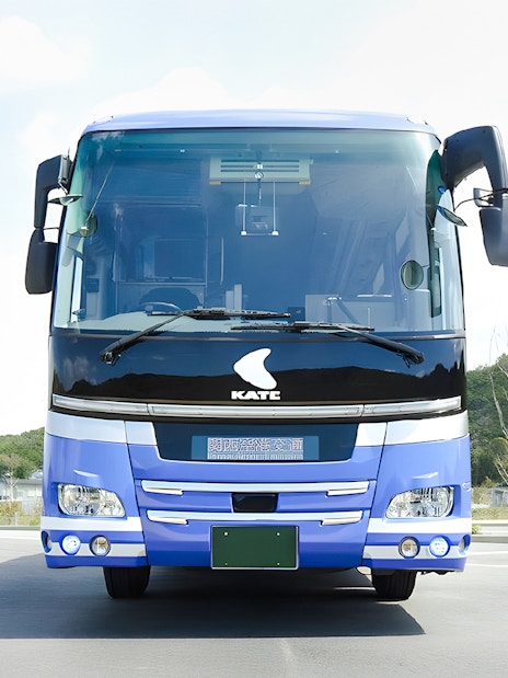 Kansai Airport transfer bus parked in lot with green hills in background.