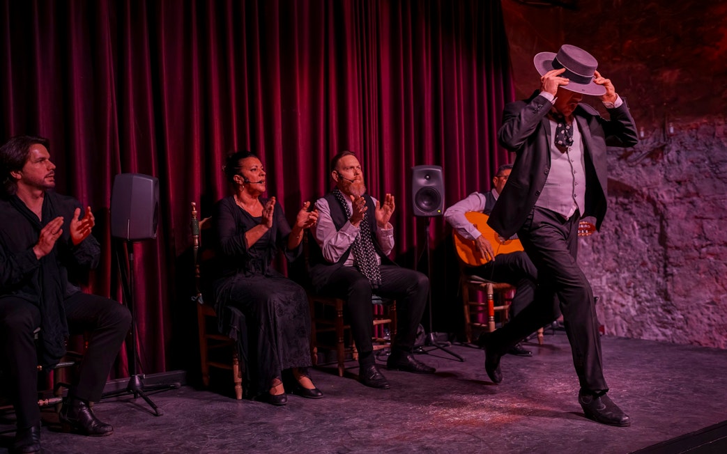 Flamenco dancer performing at Palau Dalmases with musicians clapping and playing guitar.