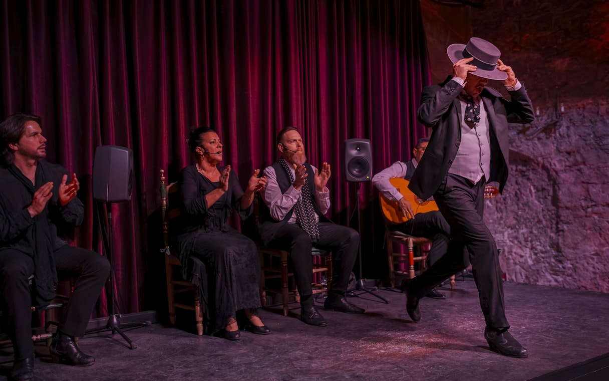 Flamenco dancer performing at Palau Dalmases with musicians clapping and playing guitar.