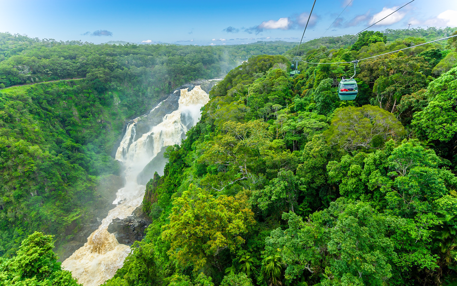 Skyrail cable car gliding over Kuranda Rainforest with waterfall view.