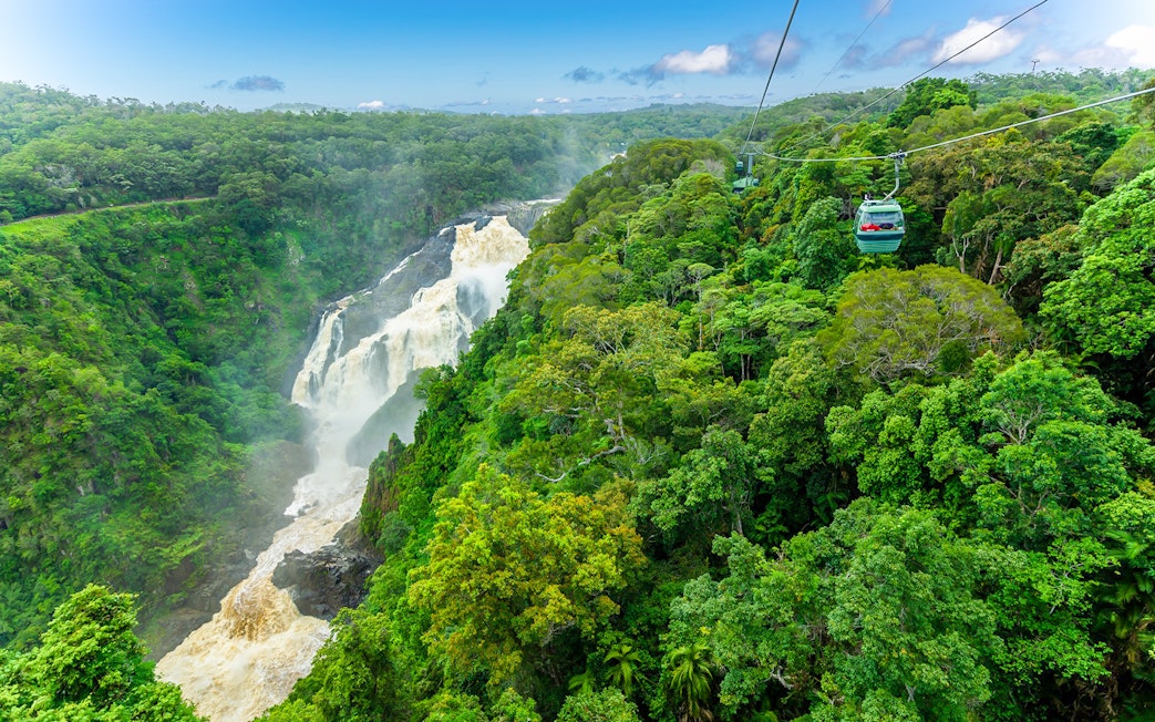 Skyrail cable car gliding over Kuranda Rainforest with waterfall view.