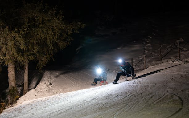 Group sledding at night with headlamps in snowy Interlaken.