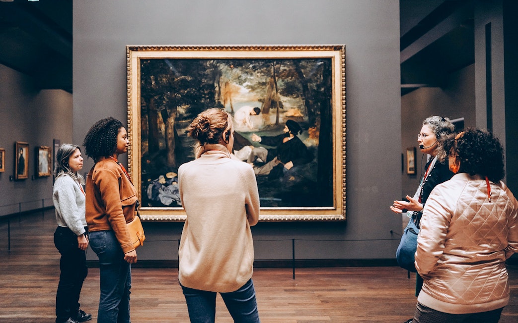 Tour guide with tourists viewing a painting inside Orsay Museum, Paris.