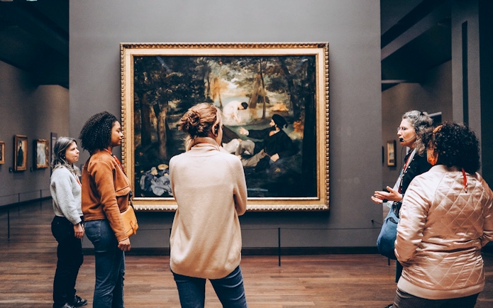 Tour guide with tourists viewing a painting inside Orsay Museum, Paris.