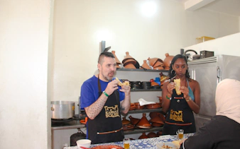 Participants tasting food during a Moroccan cooking class in Agadir, with tagines in the background.