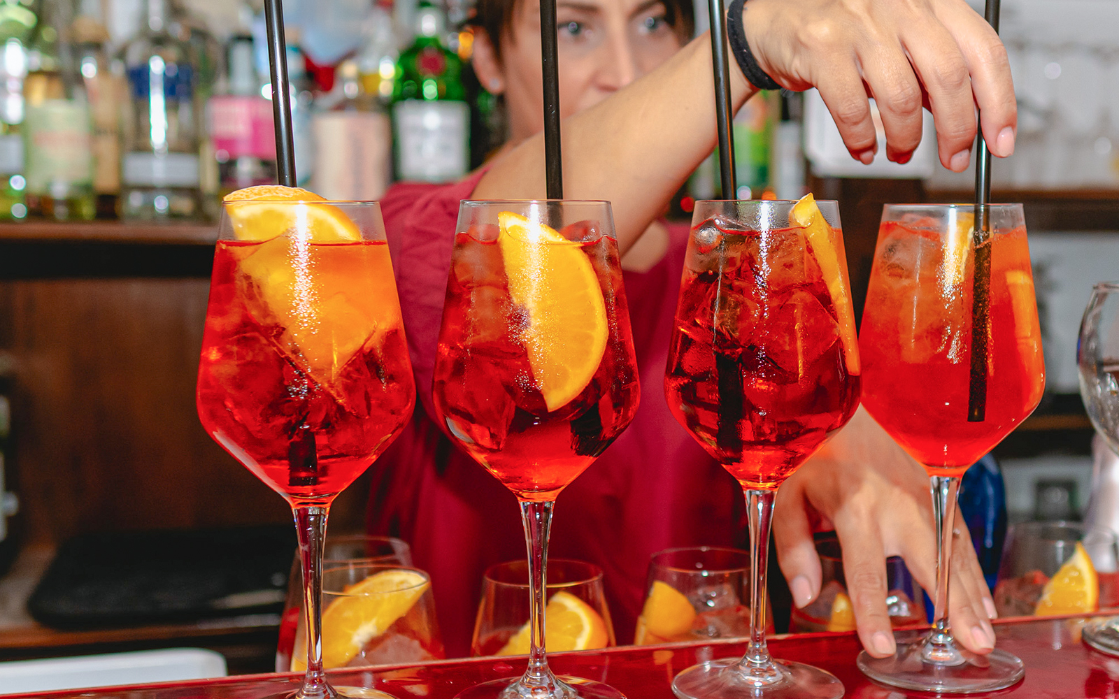 Bartender preparing Aperol Spritz cocktails at a bar.
