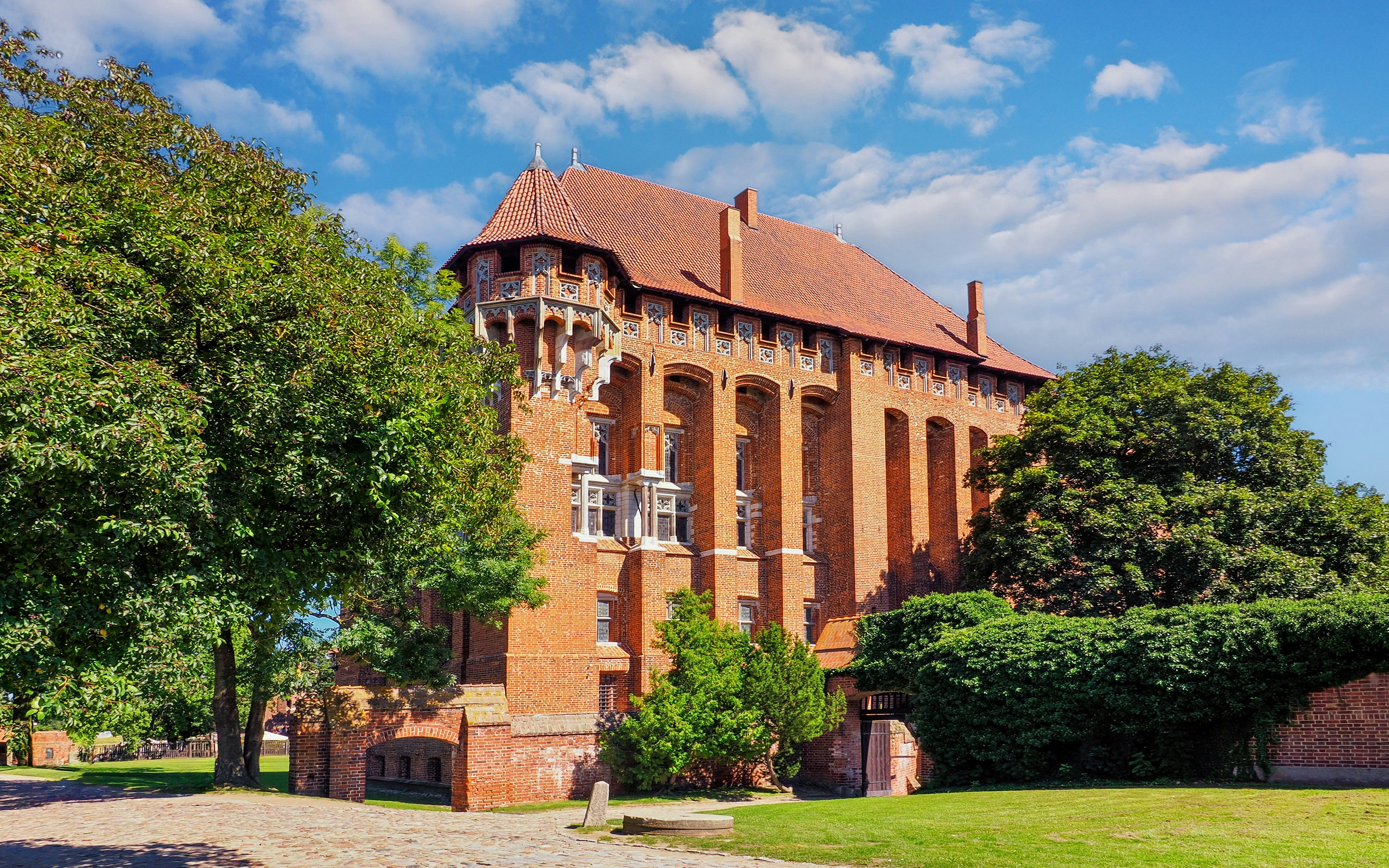 Fragment of Malbork Castle, Poland, showing Teutonic Knights' architecture and lush greenery.
