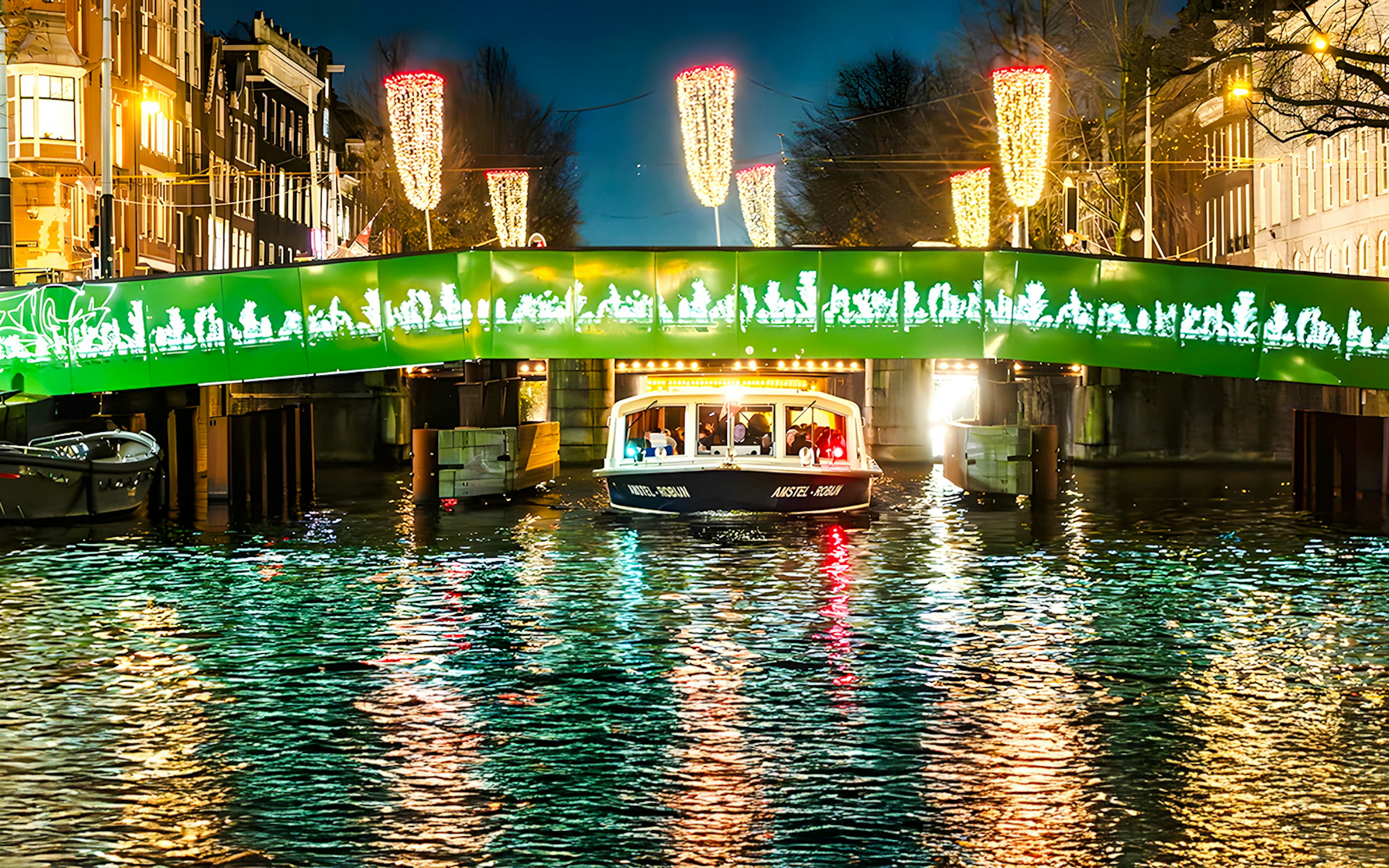 Boat passing under illuminated bridge during Amsterdam Light Festival evening cruise.