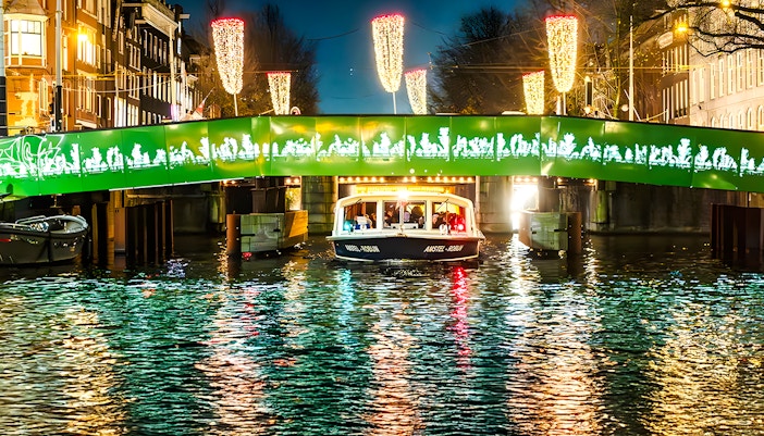 Boat passing under illuminated bridge during Amsterdam Light Festival evening cruise.
