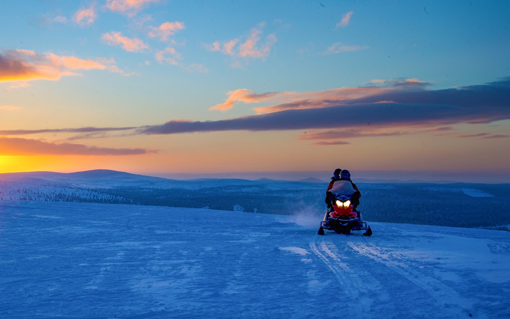 Snowmobiles on snowy terrain at sunset in Rovaniemi, Finland.