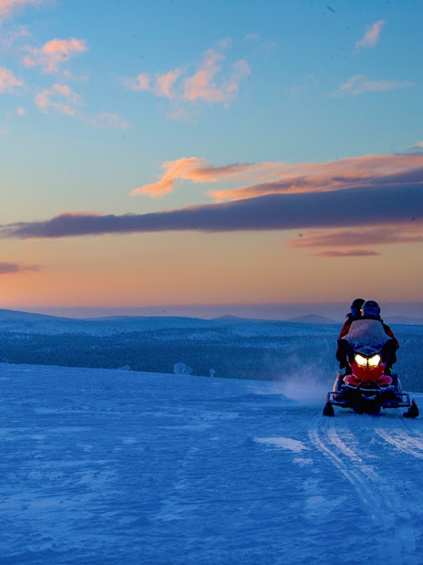 Snowmobiles on snowy terrain at sunset in Rovaniemi, Finland.