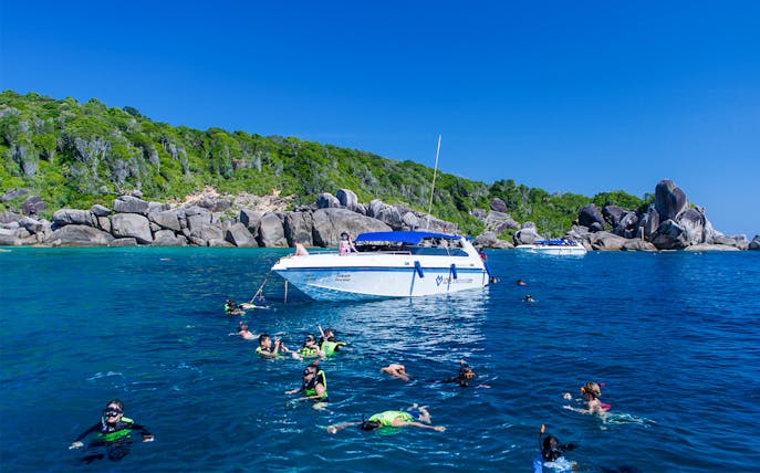 Snorkelers exploring clear waters near a boat in Loh Samah Bay, surrounded by rocky cliffs.