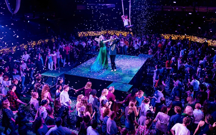 Performers on stage during "A Midsummer Night's Dream" at a seated venue, surrounded by audience.