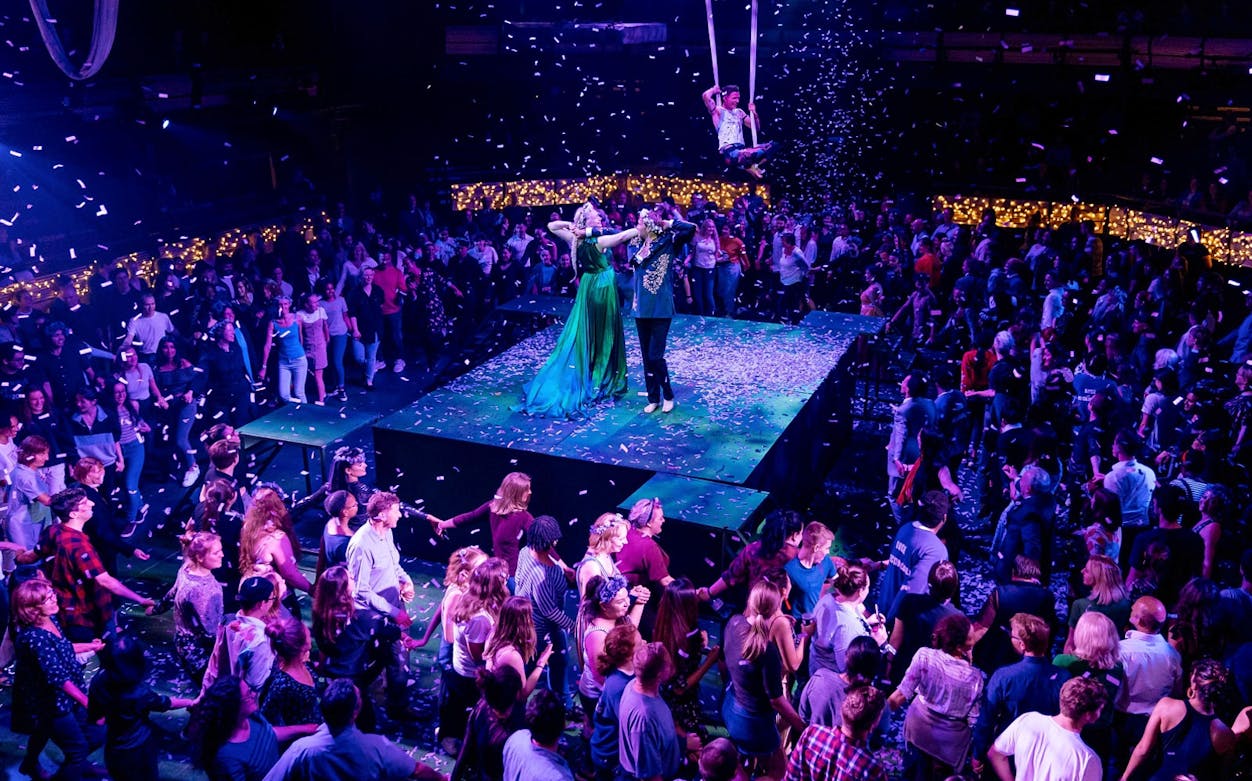 Performers on stage during "A Midsummer Night's Dream" at a seated venue, surrounded by audience.