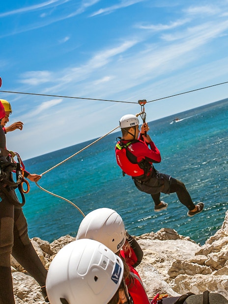 Participants zip-lining over coastal cliffs during a coasteering adventure.