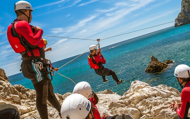 Participants zip-lining over coastal cliffs during a coasteering adventure.