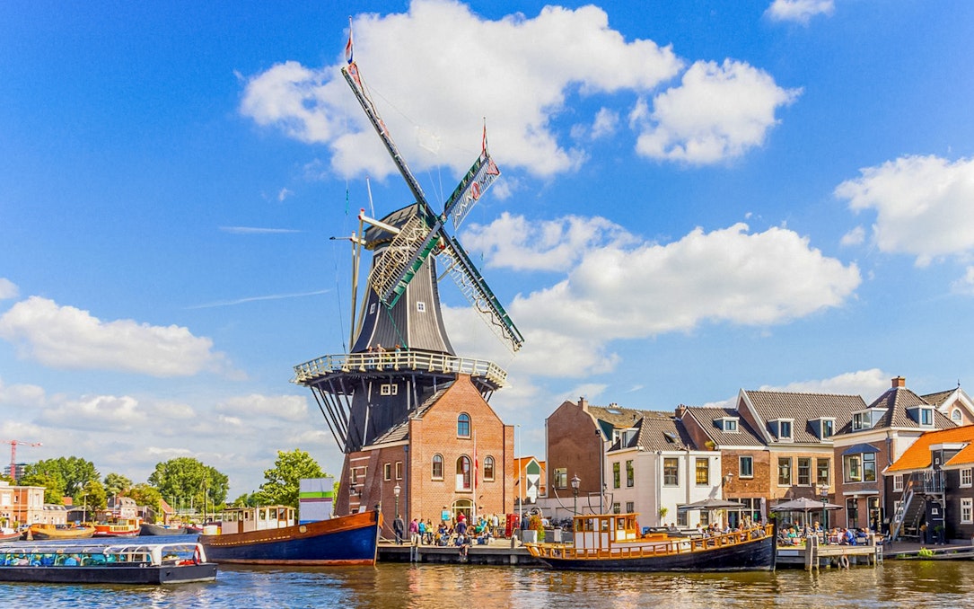 Canal cruise passing a traditional windmill on the Spaarne River in Haarlem, Netherlands.