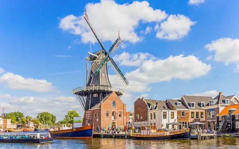 Canal cruise passing a traditional windmill on the Spaarne River in Haarlem, Netherlands.