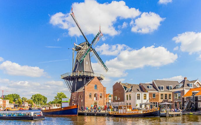 Canal cruise passing a traditional windmill on the Spaarne River in Haarlem, Netherlands.