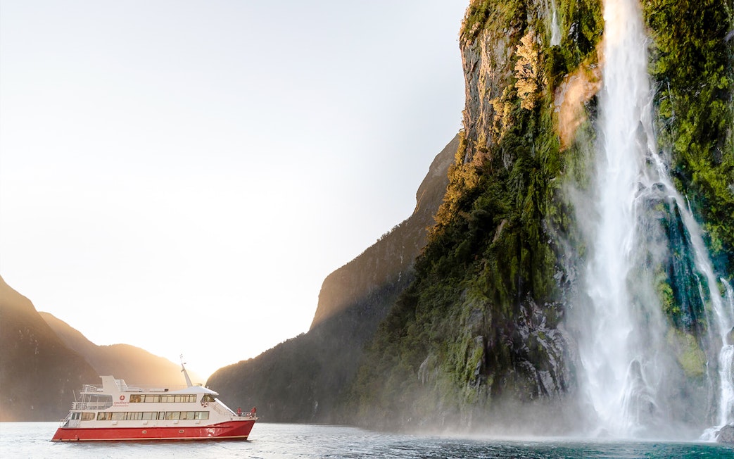 Cruise boat near waterfall in Milford Sound, New Zealand.