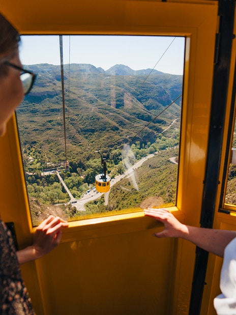 Tourists enjoying a cable car ride with views of Montserrat mountains.