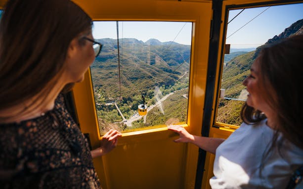 Tourists enjoying a cable car ride with views of Montserrat mountains.