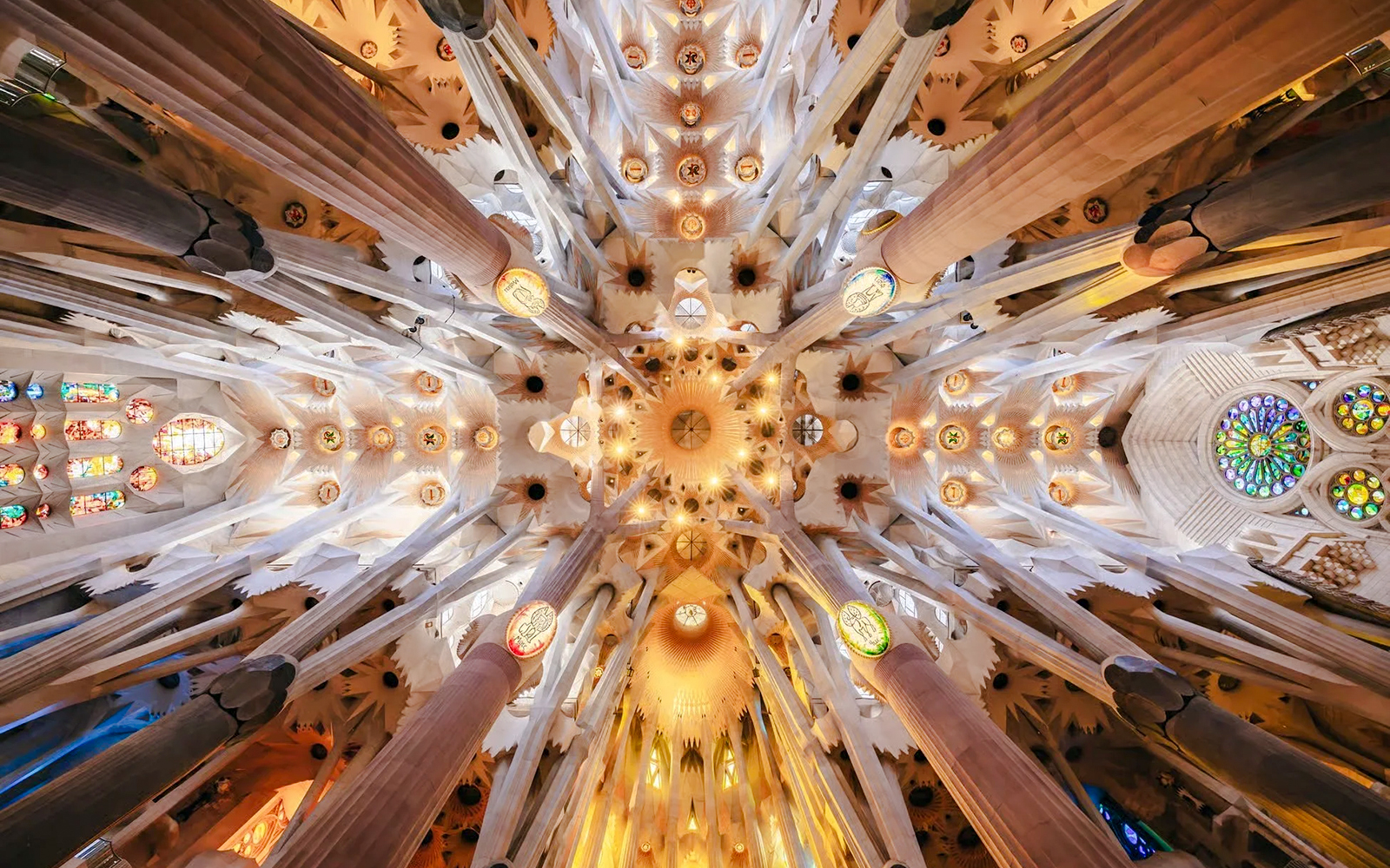 Ceiling view of Sagrada Familia with intricate columns and stained glass, Barcelona.
