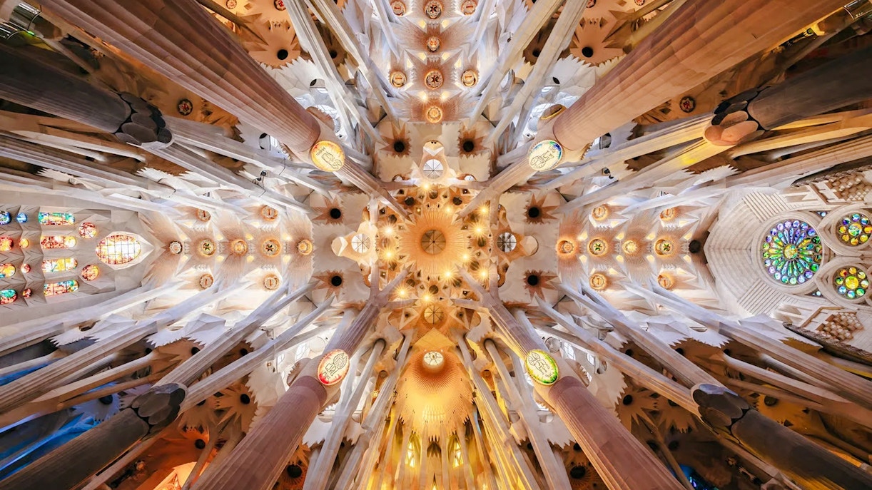 Ceiling view of Sagrada Familia with intricate columns and stained glass, Barcelona.