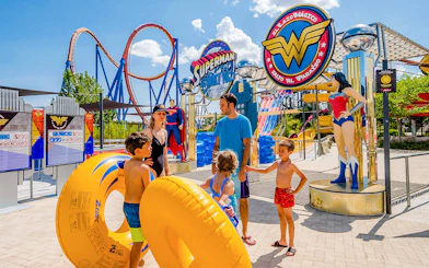 Parque Warner Madrid entrance with Superman and Wonder Woman statues, vibrant theme park atmosphere.