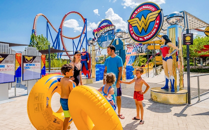 Parque Warner Madrid entrance with Superman and Wonder Woman statues, vibrant theme park atmosphere.