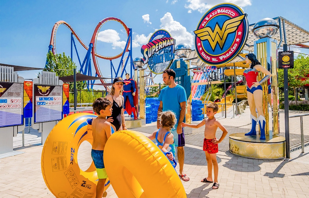 Parque Warner Madrid entrance with Superman and Wonder Woman statues, vibrant theme park atmosphere.