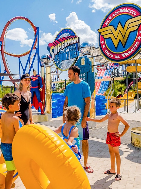 Parque Warner Madrid entrance with Superman and Wonder Woman statues, vibrant theme park atmosphere.