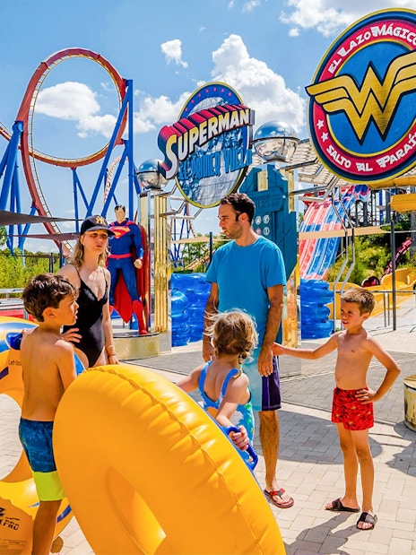 Parque Warner Madrid entrance with Superman and Wonder Woman statues, vibrant theme park atmosphere.