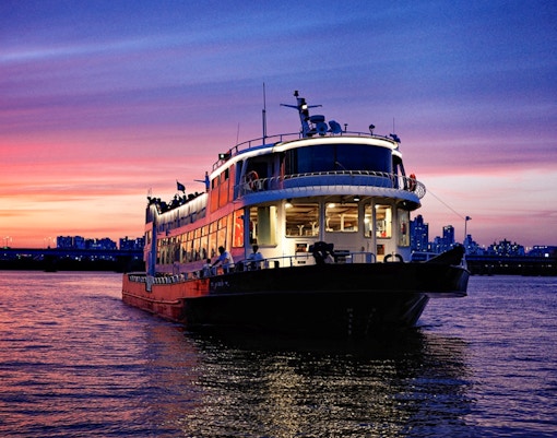 Han River cruise boat at sunset with city skyline in the background.