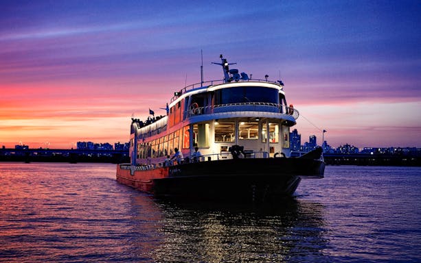 Han River cruise boat at sunset with city skyline in the background.