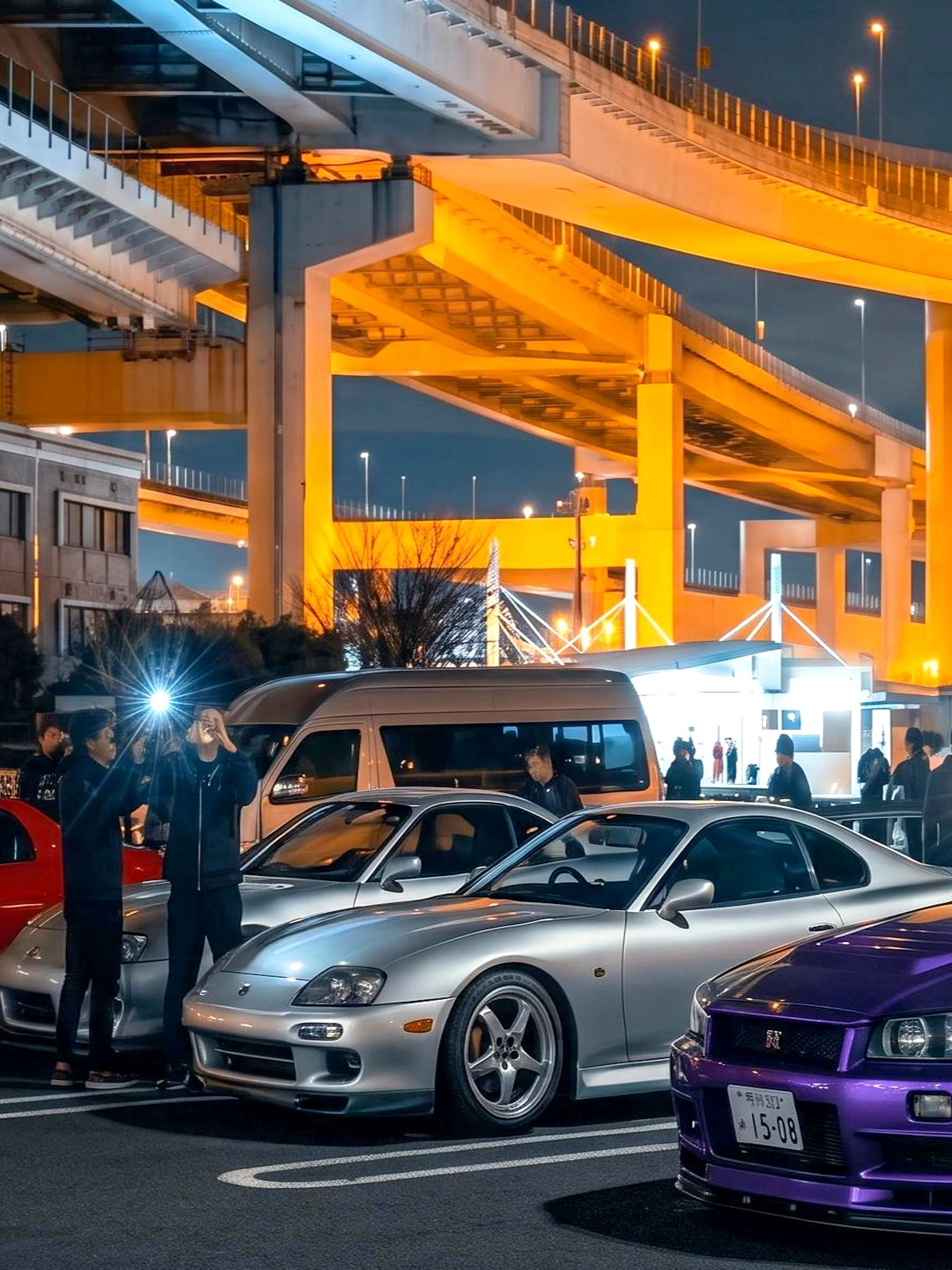 Skyline R34 and other cars at Daikoku PA car meeting, Japan, under illuminated highway.