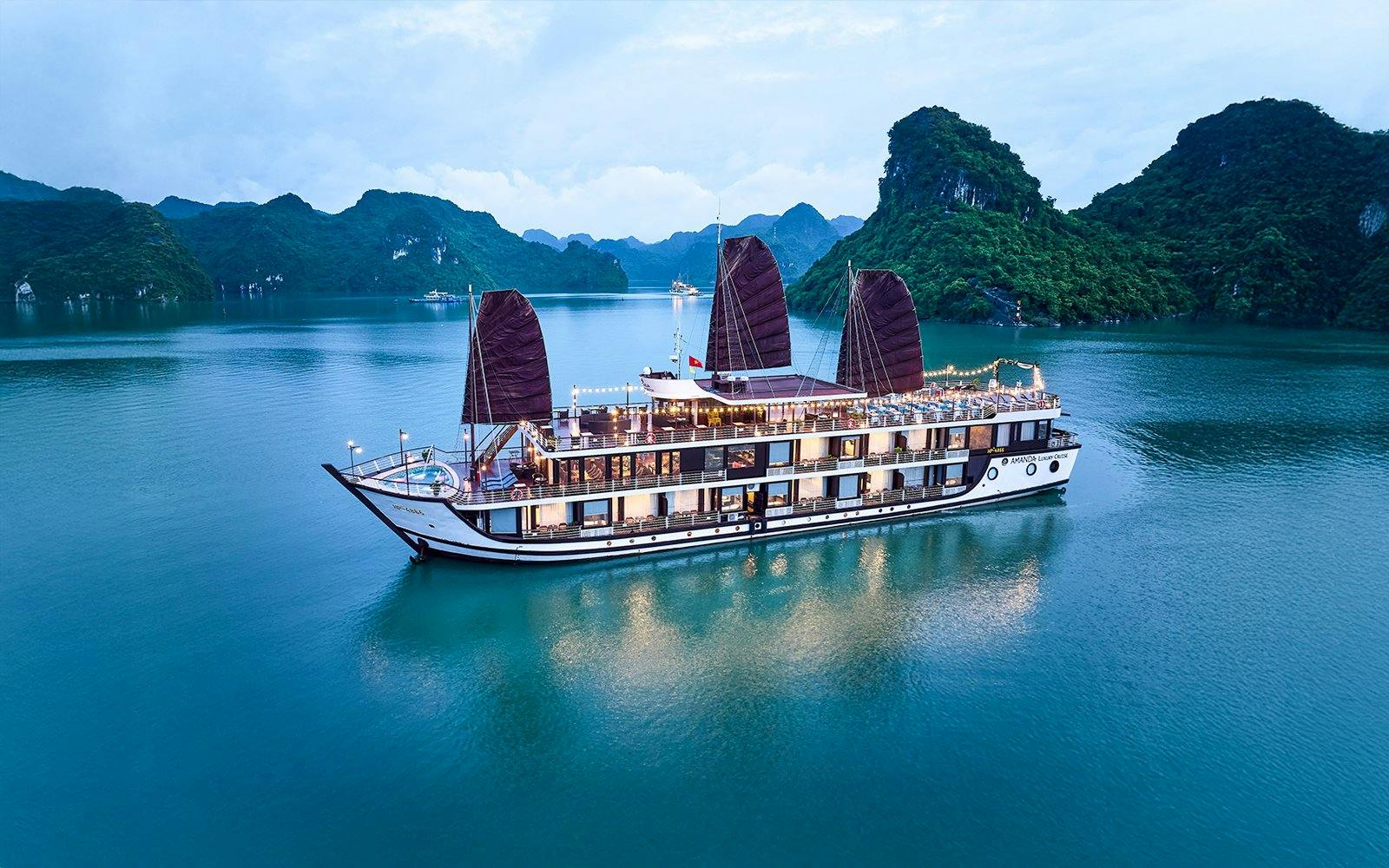Aerial view of Amanda Luxury Cruise sailing in Halong Bay at dusk.