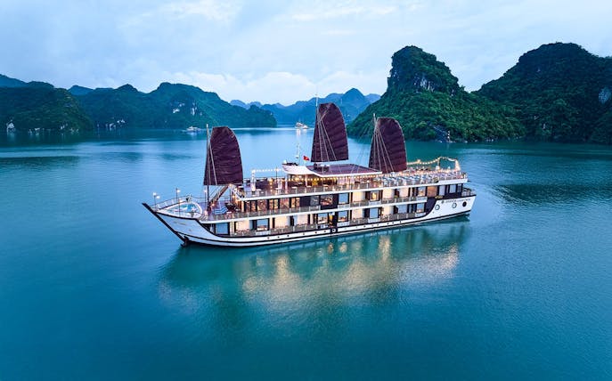 Aerial view of Amanda Luxury Cruise sailing in Halong Bay at dusk.