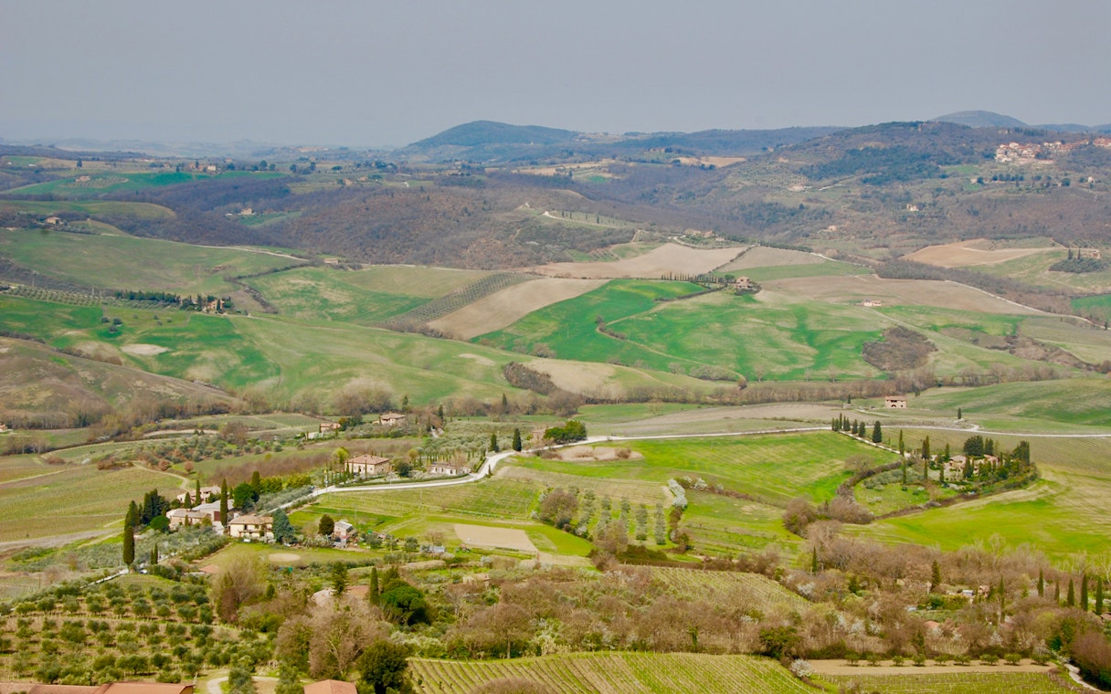 Rolling hills and vineyards in Tuscany, Italy, viewed from a distance on a clear day.