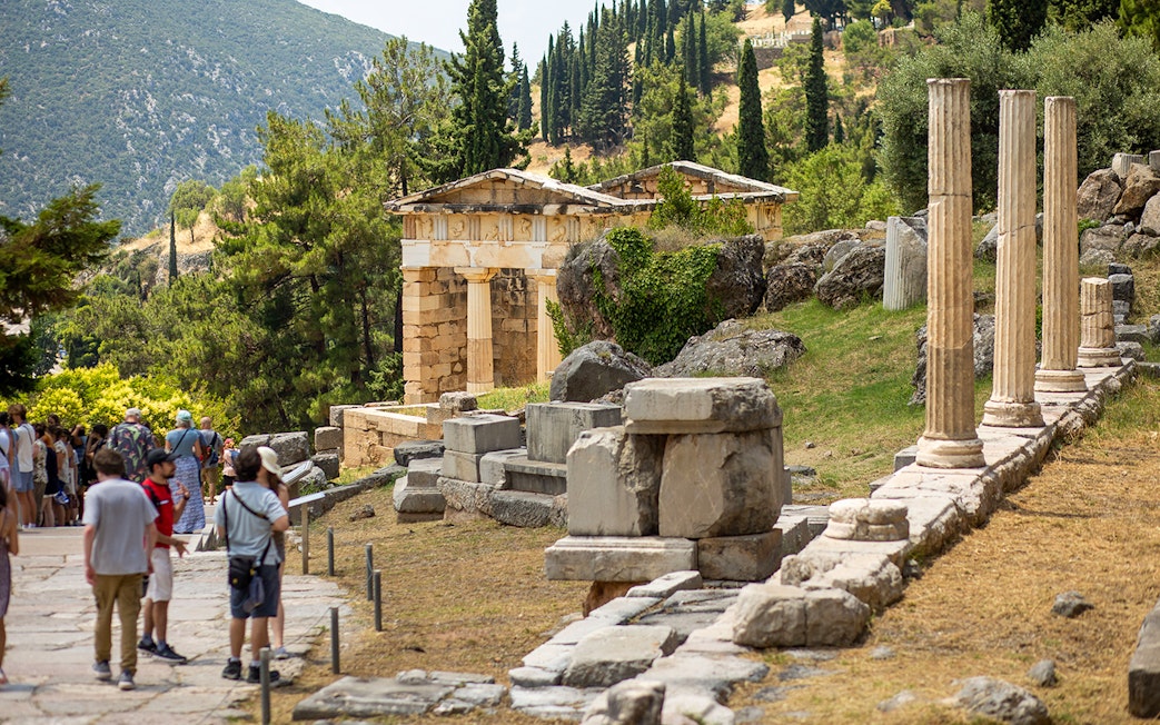 Guests exploring ancient ruins at Delphi site, Greece, with columns and temple remains.