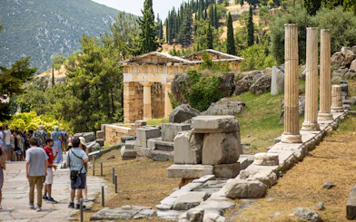 Guests exploring ancient ruins at Delphi site, Greece, with columns and temple remains.