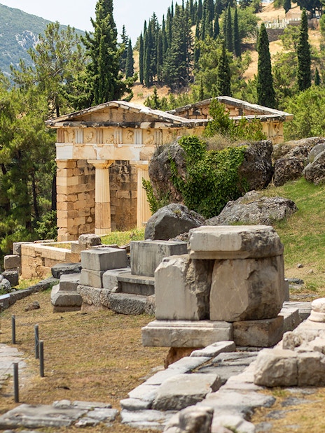Guests exploring ancient ruins at Delphi site, Greece, with columns and temple remains.