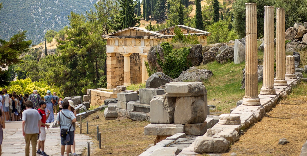 Guests exploring ancient ruins at Delphi site, Greece, with columns and temple remains.