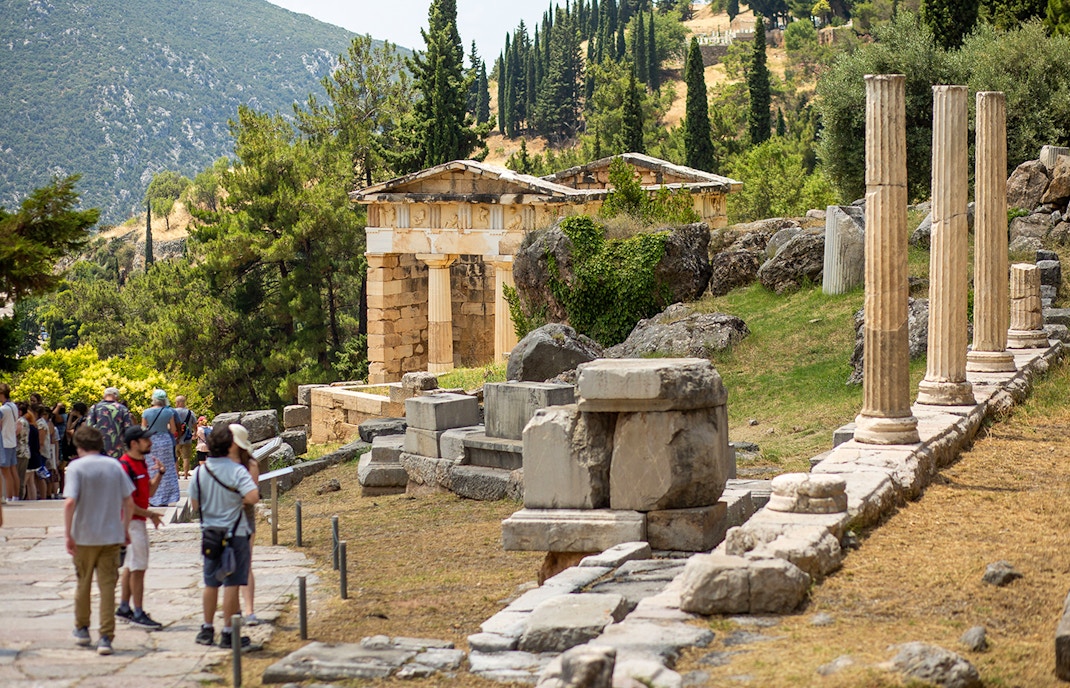 Guests exploring ancient ruins at Delphi site, Greece, with columns and temple remains.