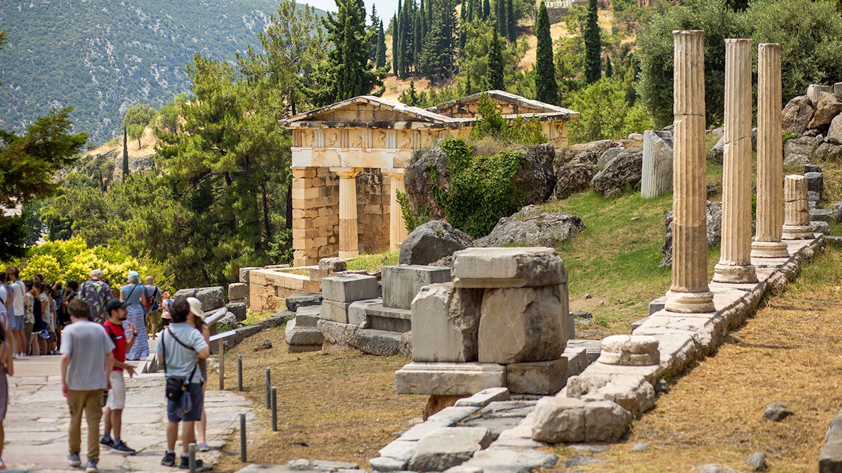 Guests exploring ancient ruins at Delphi site, Greece, with columns and temple remains.
