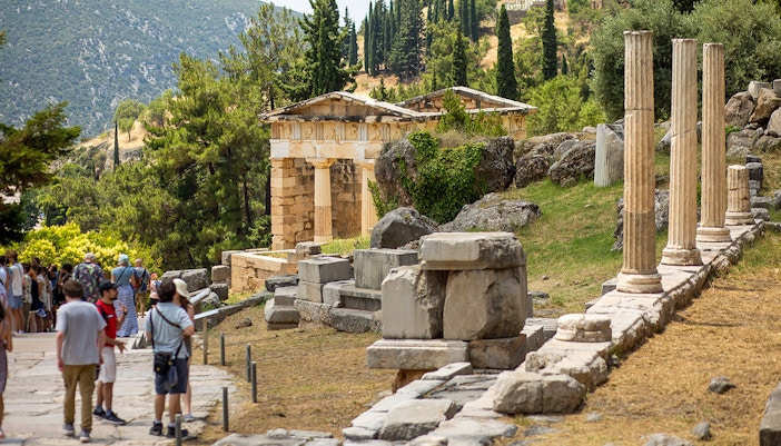 Guests exploring ancient ruins at Delphi site, Greece, with columns and temple remains.